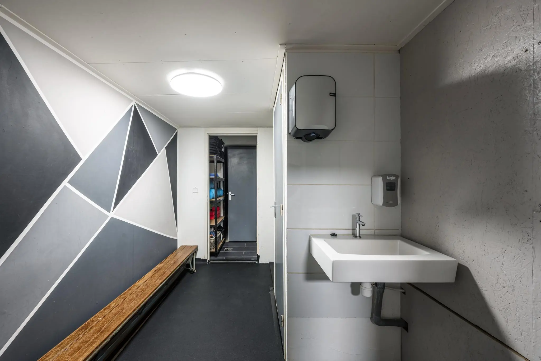 Kleedruimte aan de Albert Cuypstraat met moderne wanddecoratie, houten bank, en een wasbak met zeepdispenser.